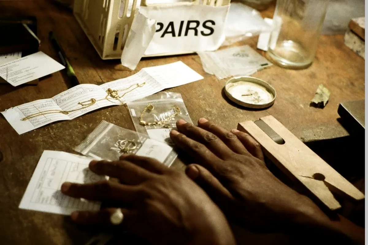 Hands working at Thabile's jewellery bench surrounded by tools and materials.