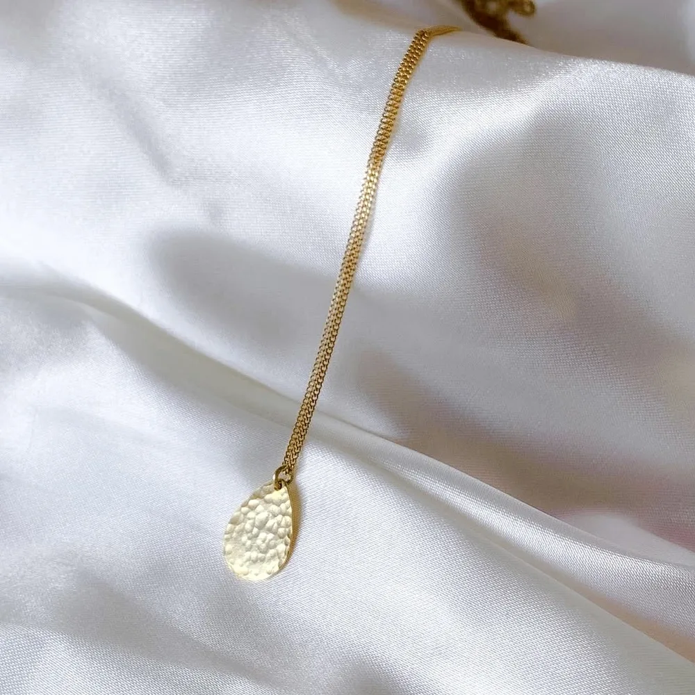 Close detail of a hammered circular pendant necklace on pale satin.