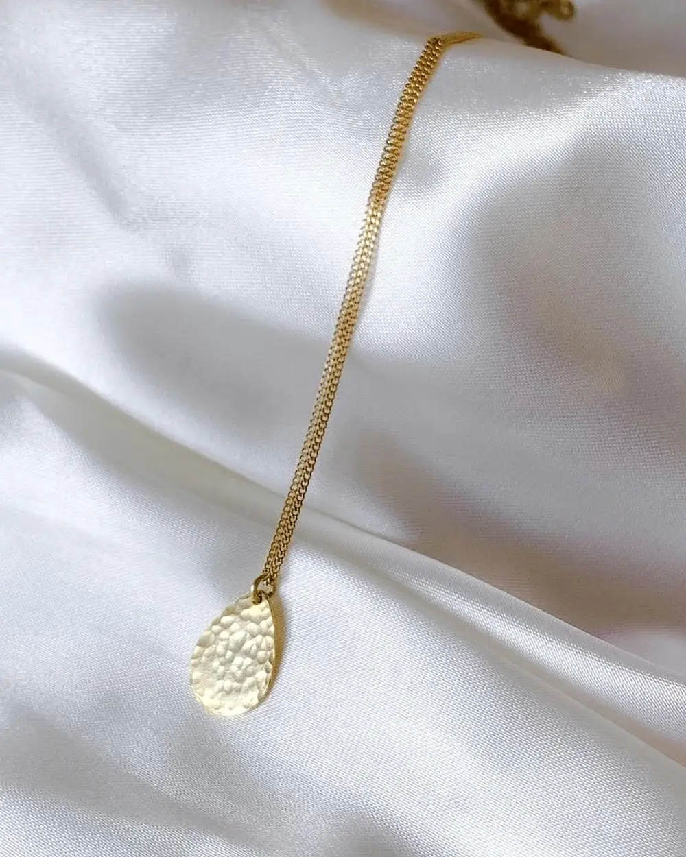 Hammered circular pendant necklace on pale satin.