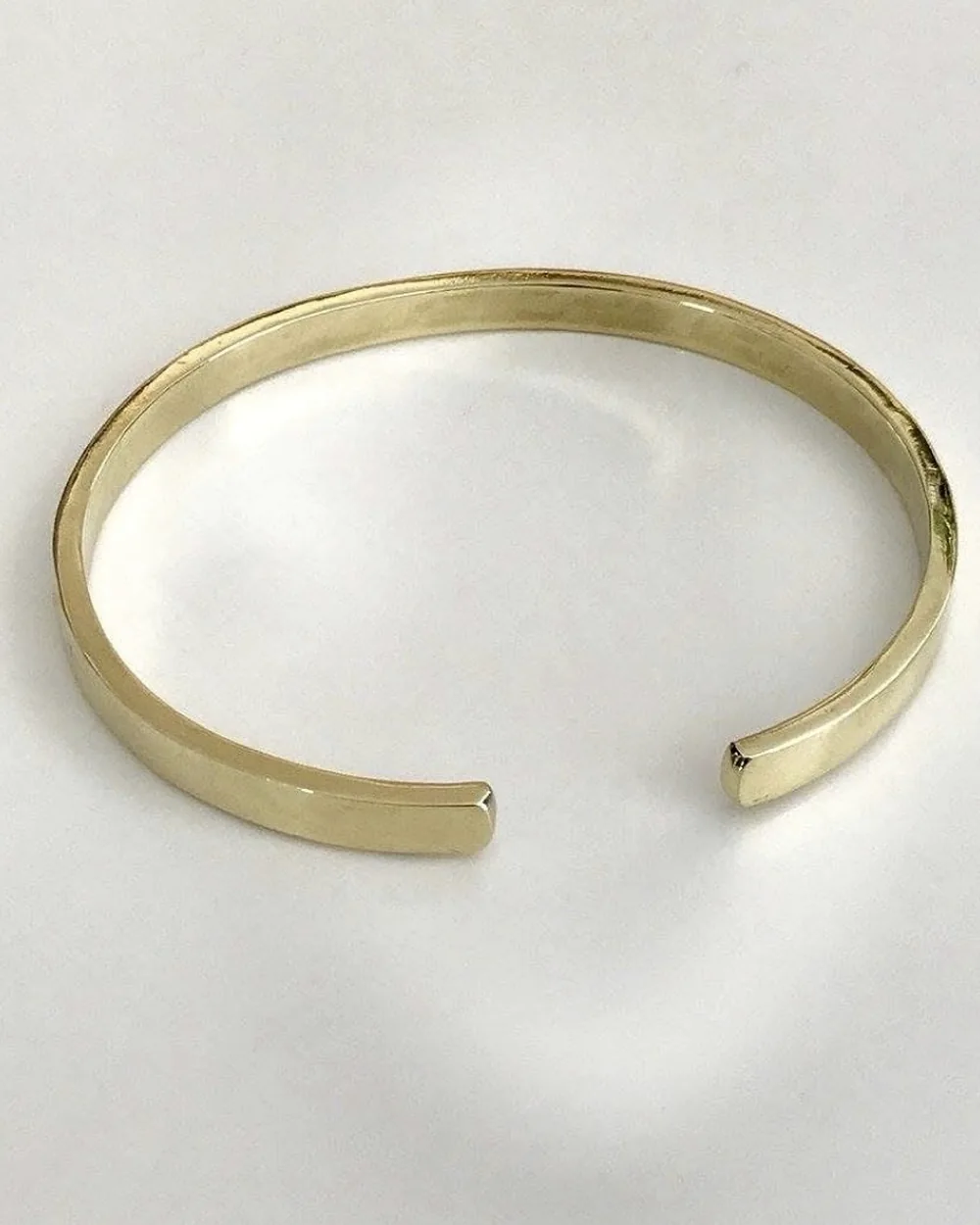 Open gold-tone bangle on a clean pale background.