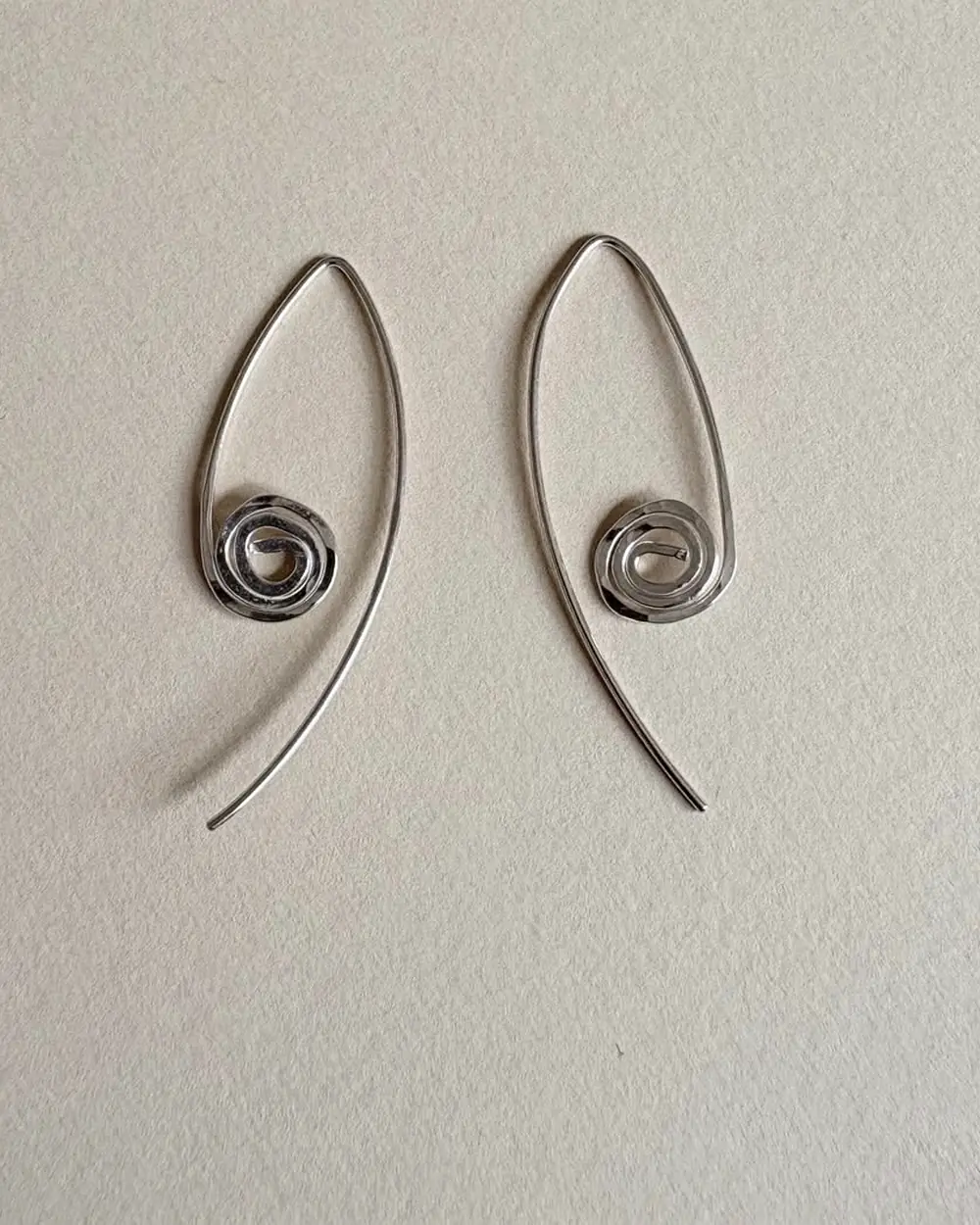 Pair of spiral drop earrings arranged side by side on a neutral surface.